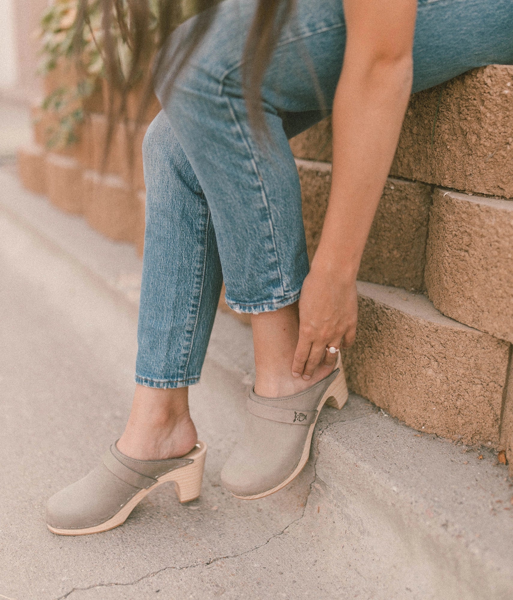 woman wearing blue jeans with high rise clog mules in stone grey nubuck leather on a light wooden base