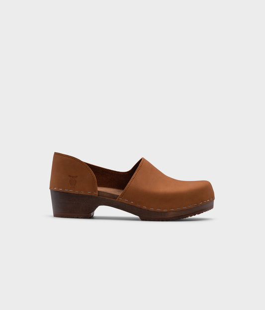 low heeled closed-back clogs in light brown nubuck leather stapled on a dark wooden base