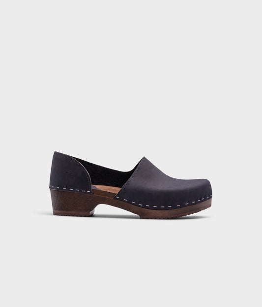 low heeled closed-back clogs in navy blue nubuck leather stapled on a dark wooden base