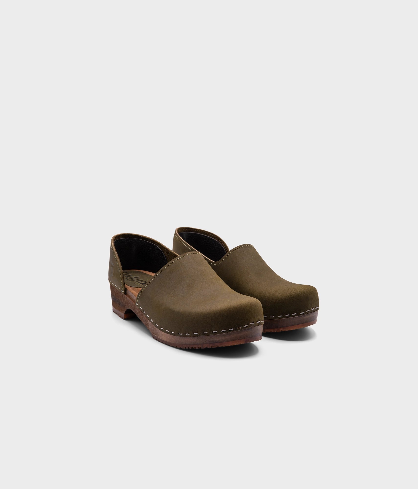 low heeled closed-back clogs in olive green nubuck leather stapled on a dark wooden base