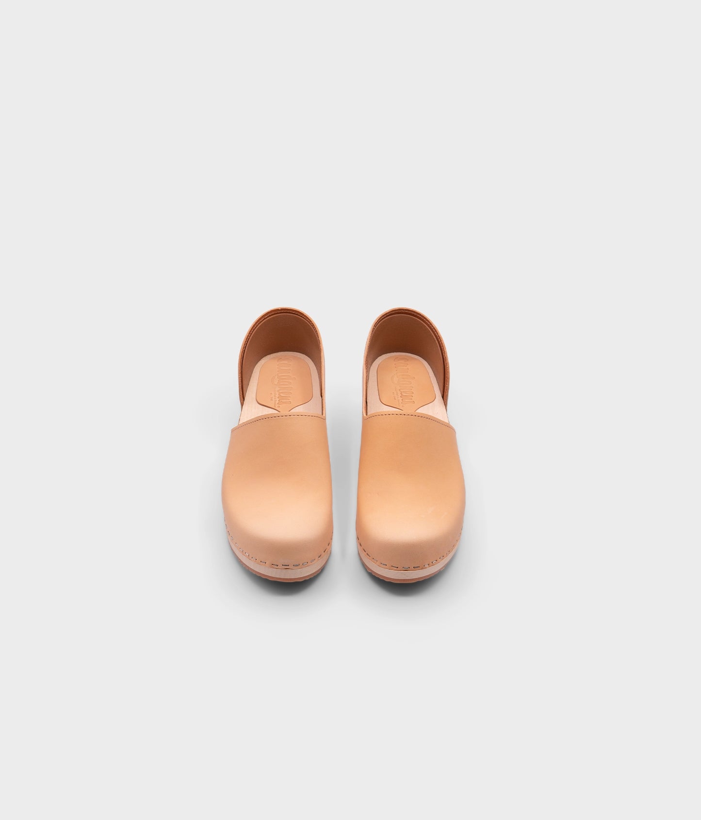 low heeled closed-back clogs in beige vegetable tanned leather stapled on a light wooden base