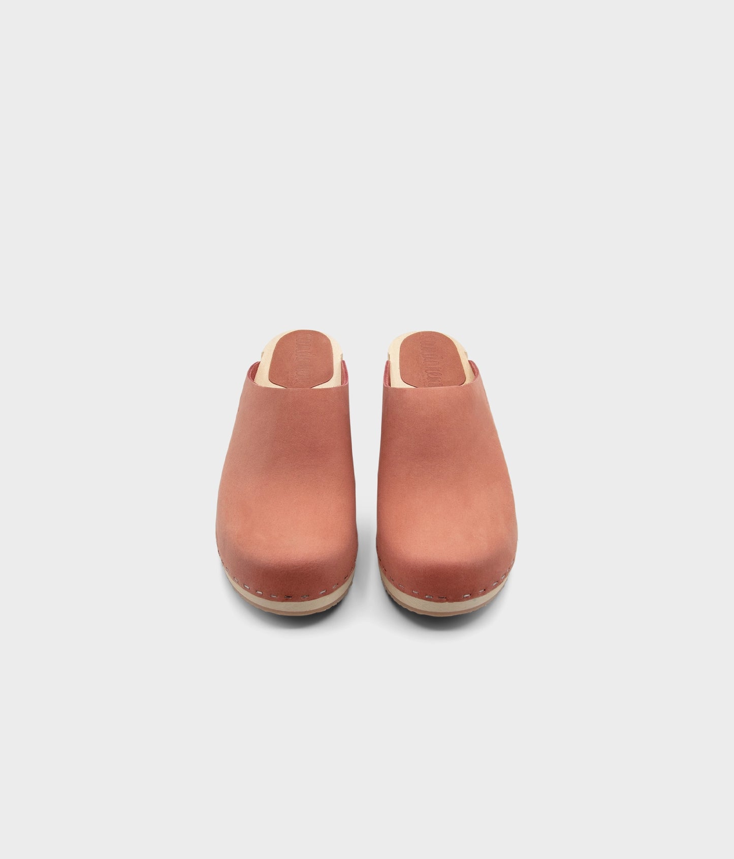 low heeled minimalistic clog mules in blush pink nubuck leather stapled on a light wooden base
