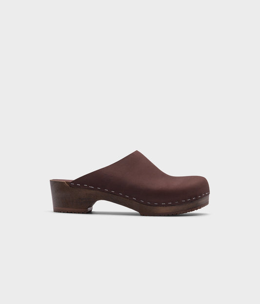 low heeled minimalistic clog mules in fudge nubuck leather stapled on a dark wooden base