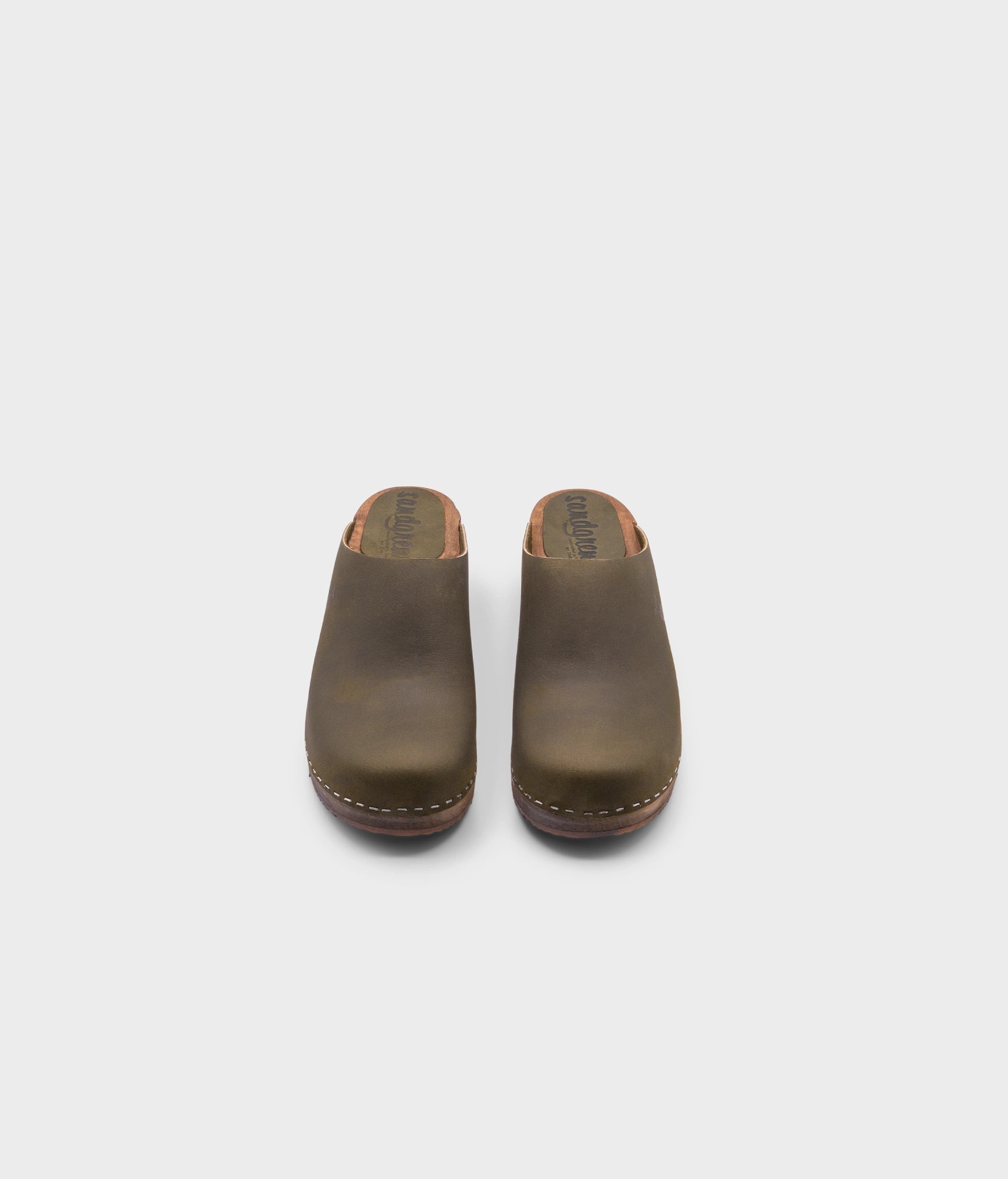 low heeled minimalistic clog mules in olive nubuck leather stapled on a dark wooden base