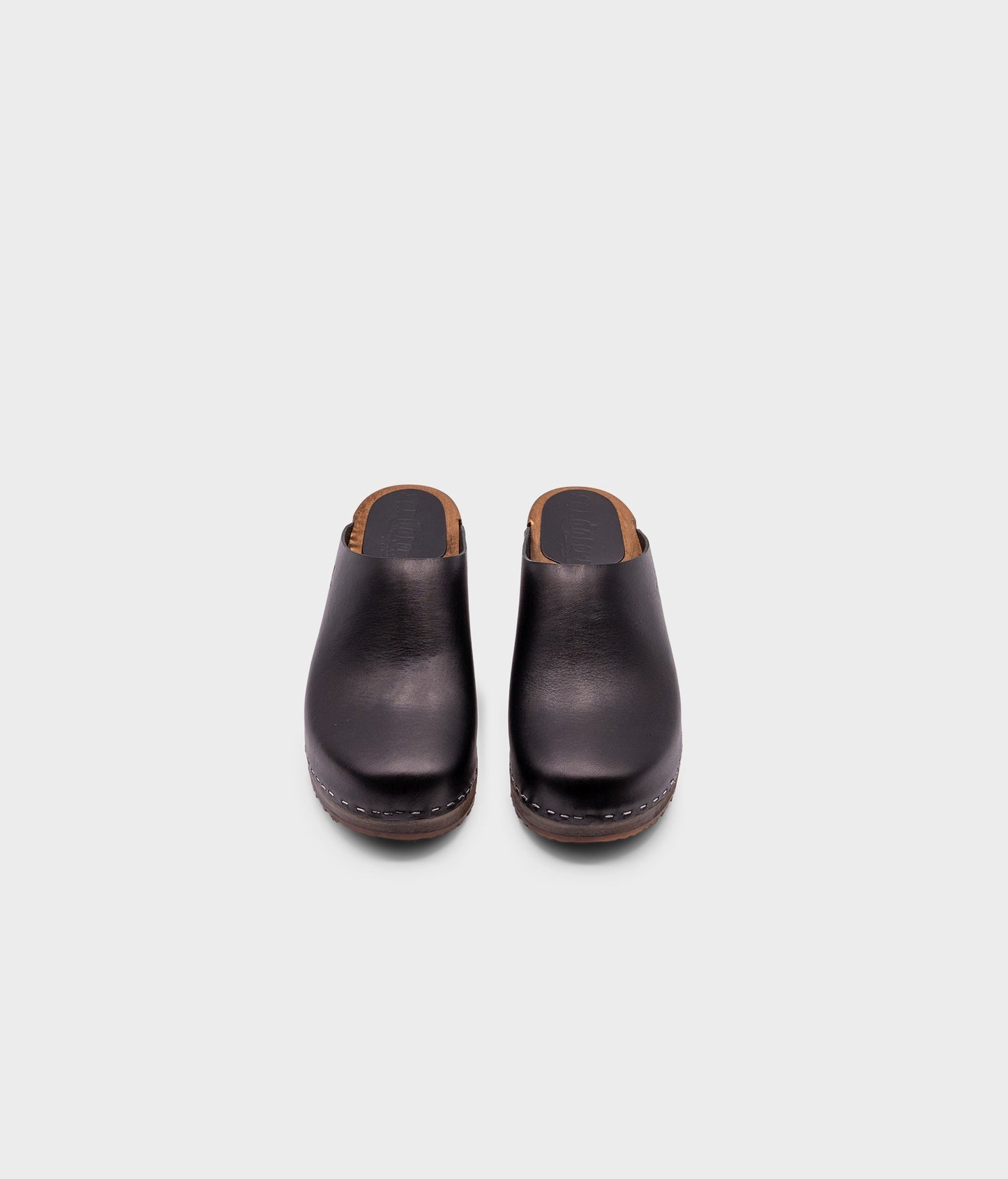 low heeled minimalistic clog mules in black vegetable tanned leather stapled on a dark wooden base