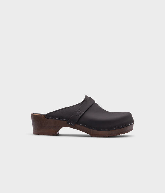 classic low heeled clog mule in black nubuck leather stapled on a dark wooden base with a leather strap