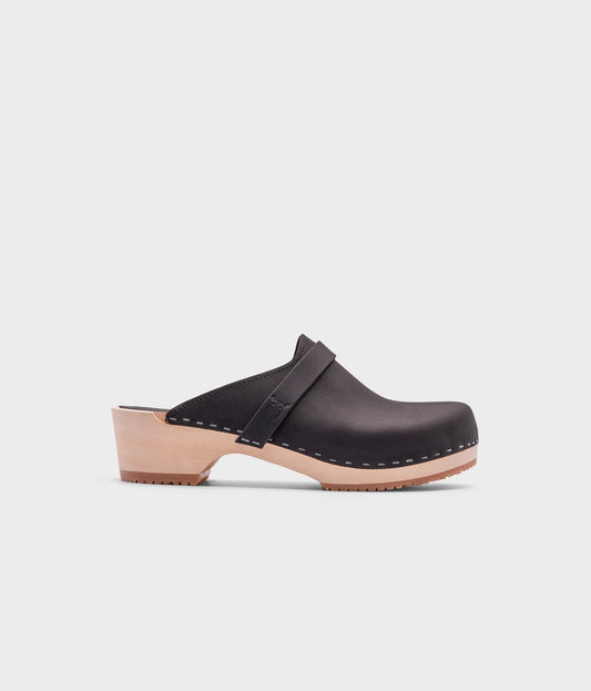 classic low heeled clog mule in black nubuck leather stapled on a light wooden base with a leather strap