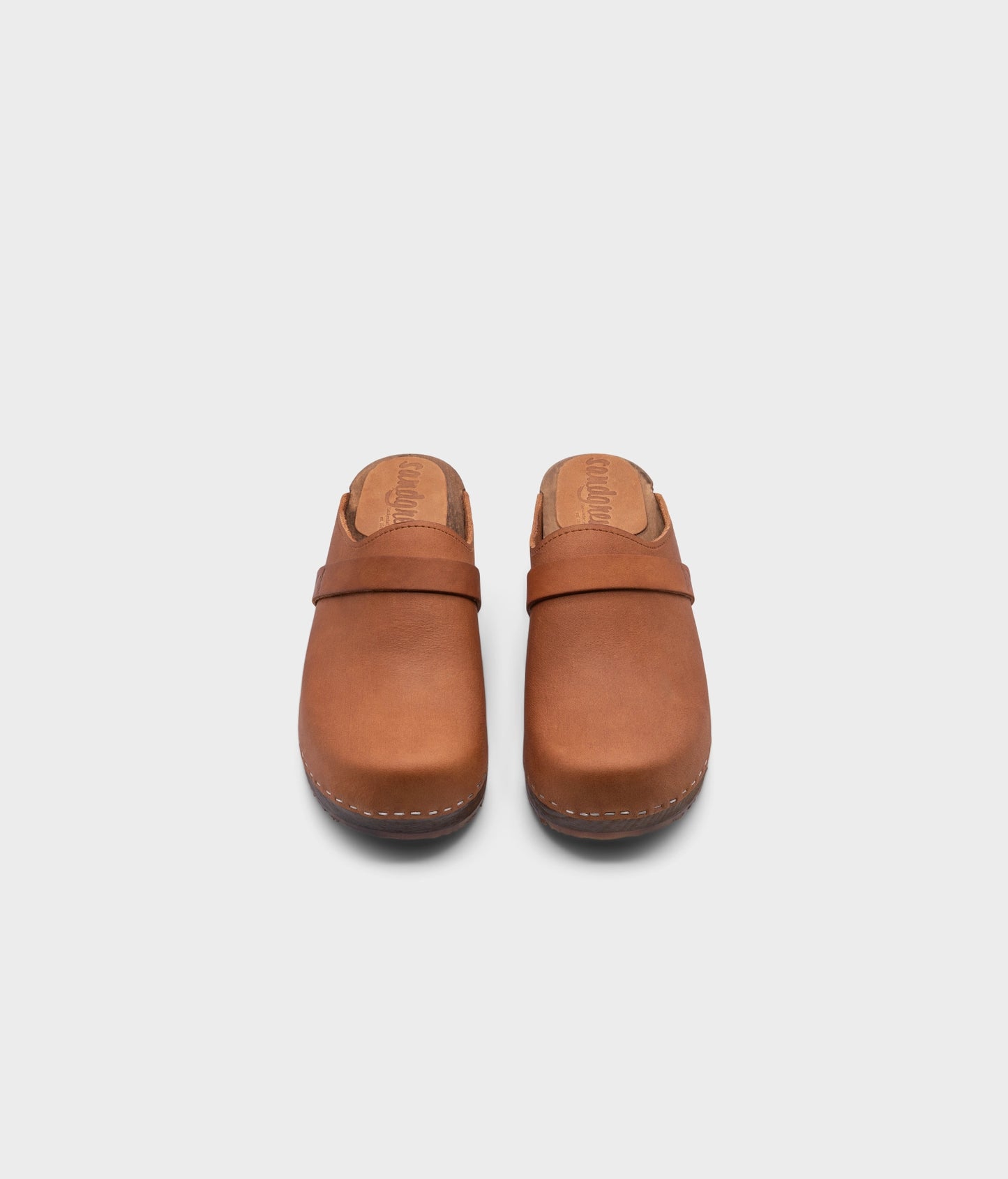 classic low heeled clog mule in light brown nubuck leather stapled on a dark wooden base with a leather strap