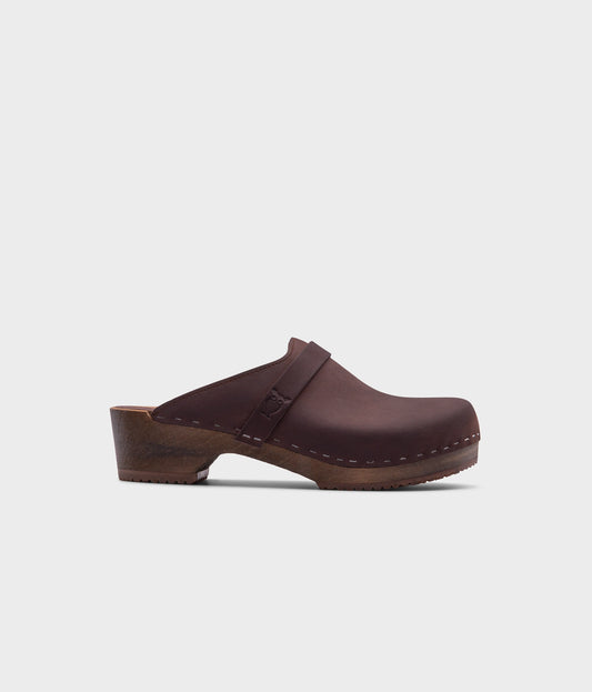 classic low heeled clog mule in dark brown nubuck leather stapled on a dark wooden base with a leather strap