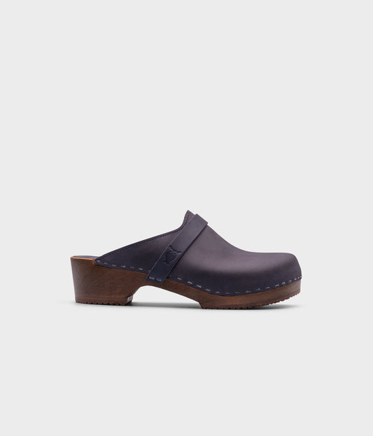 classic low heeled clog mule in navy blue nubuck leather stapled on a dark wooden base with a leather strap