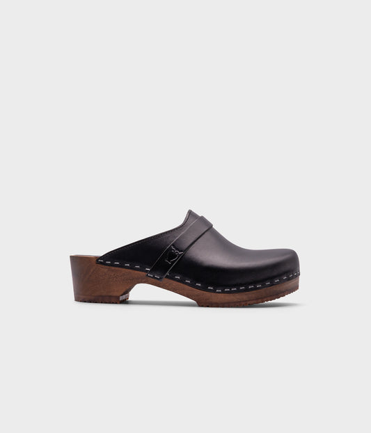 classic low heeled clog mule in black vegetable tanned leather stapled on a dark wooden base with a leather strap