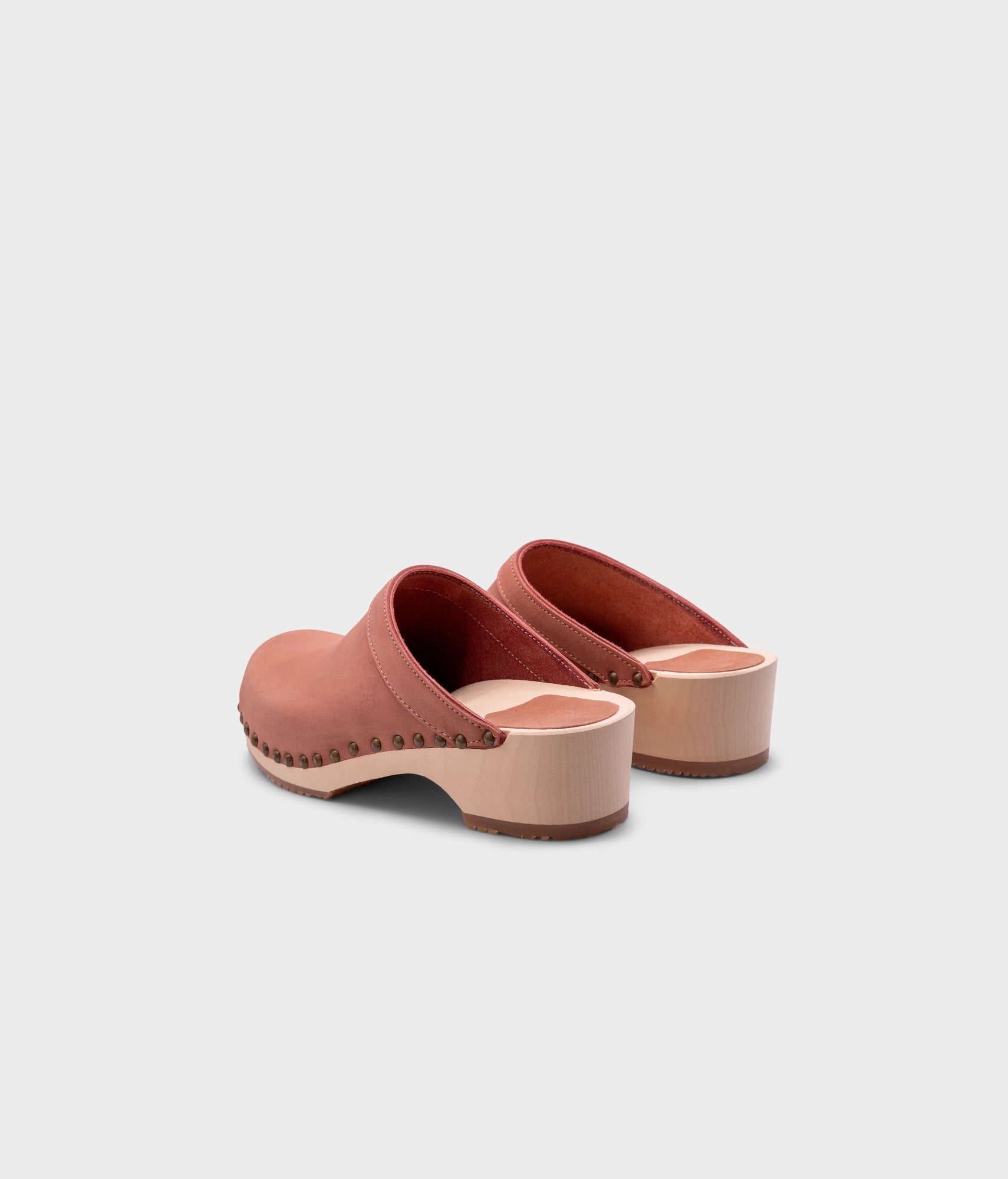 low heeled clog mules in blush pink nubuck leather stapled on a light wooden base with brass gold studs