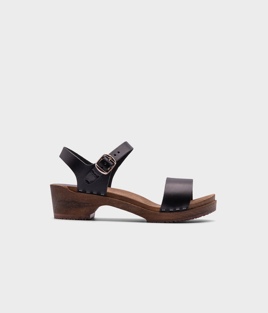low heeled open-toe clog sandal in black vegetable tanned leather stapled on a dark wooden base