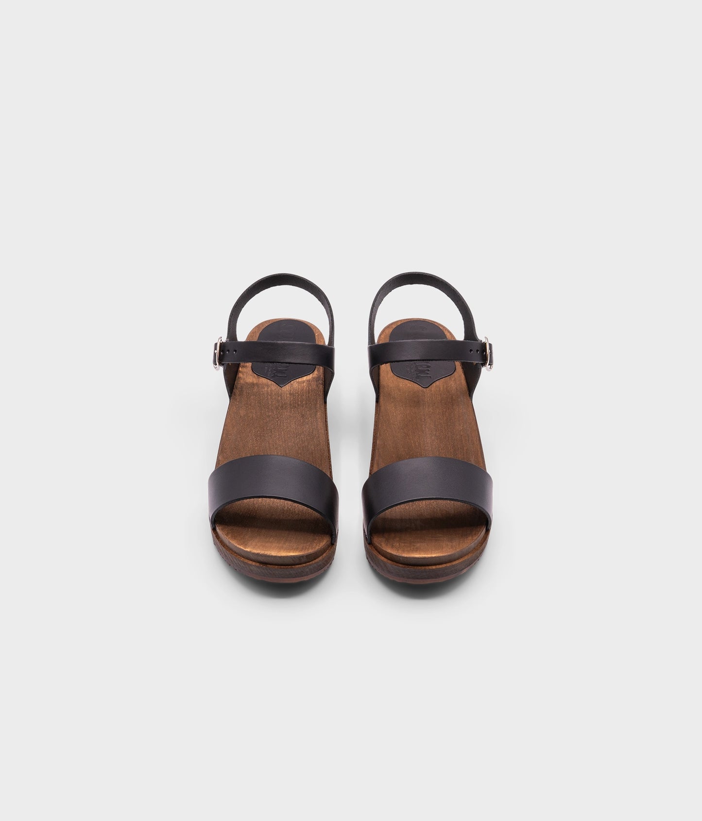 low heeled open-toe clog sandal in black vegetable tanned leather stapled on a dark wooden base