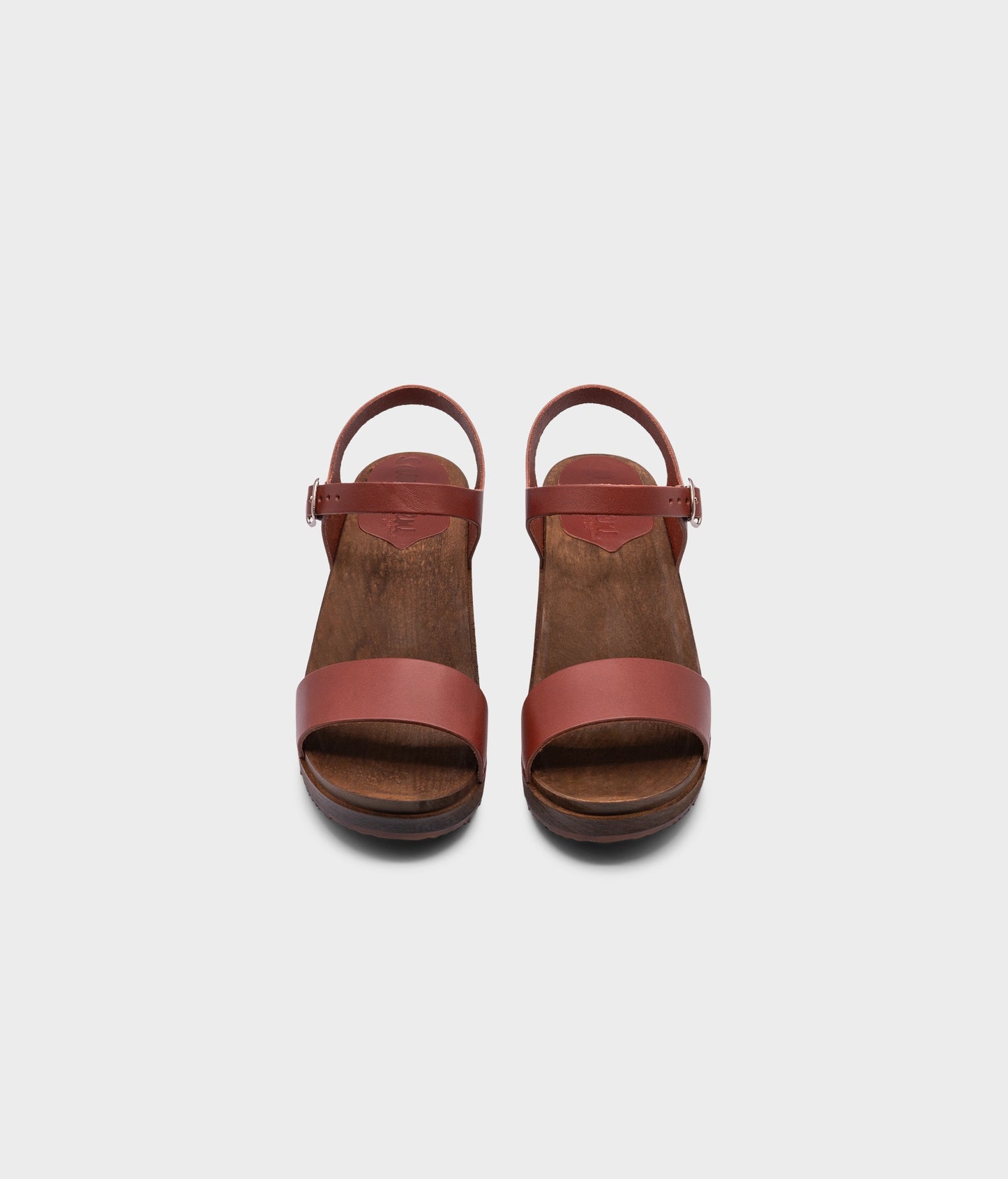 low heeled open-toe clog sandal in cognac red vegetable tanned leather stapled on a dark wooden base