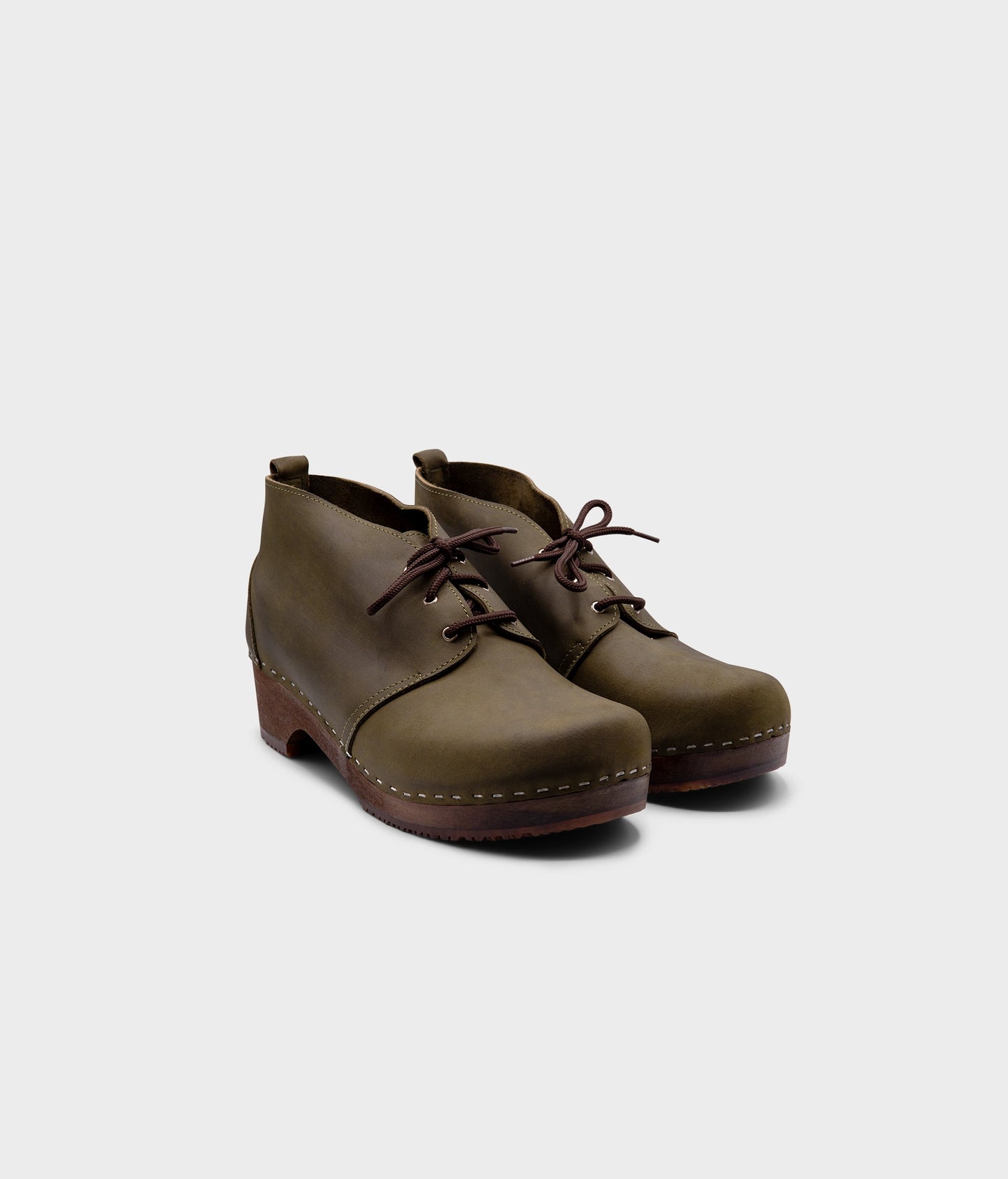 low heeled mens chukka clog boots in olive green nubuck leather stapled on a dark wooden base with brown laces