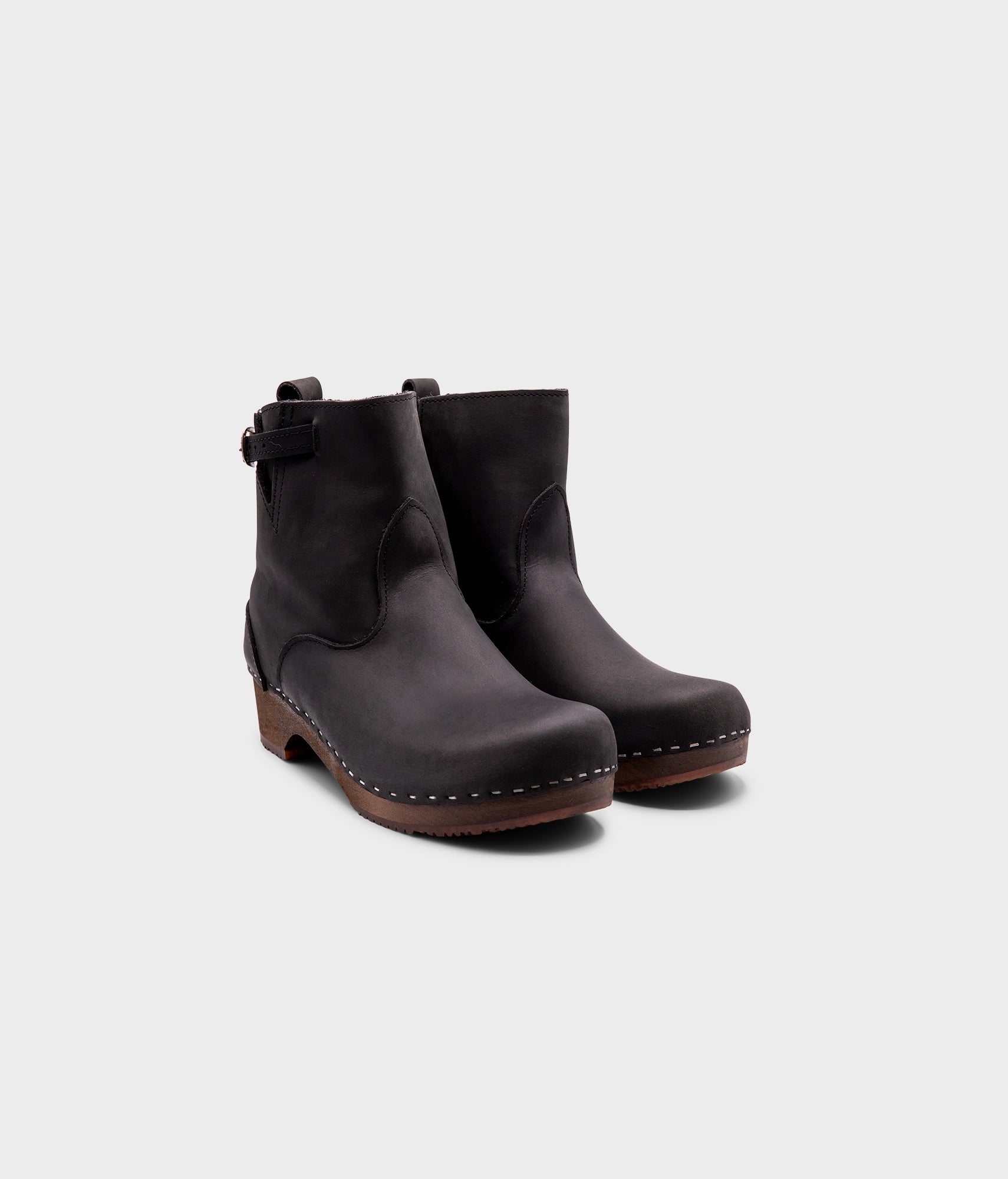 low heeled clog boots in black nubuck leather with a mid-shaft and silver buckle, stapled on a dark wooden base