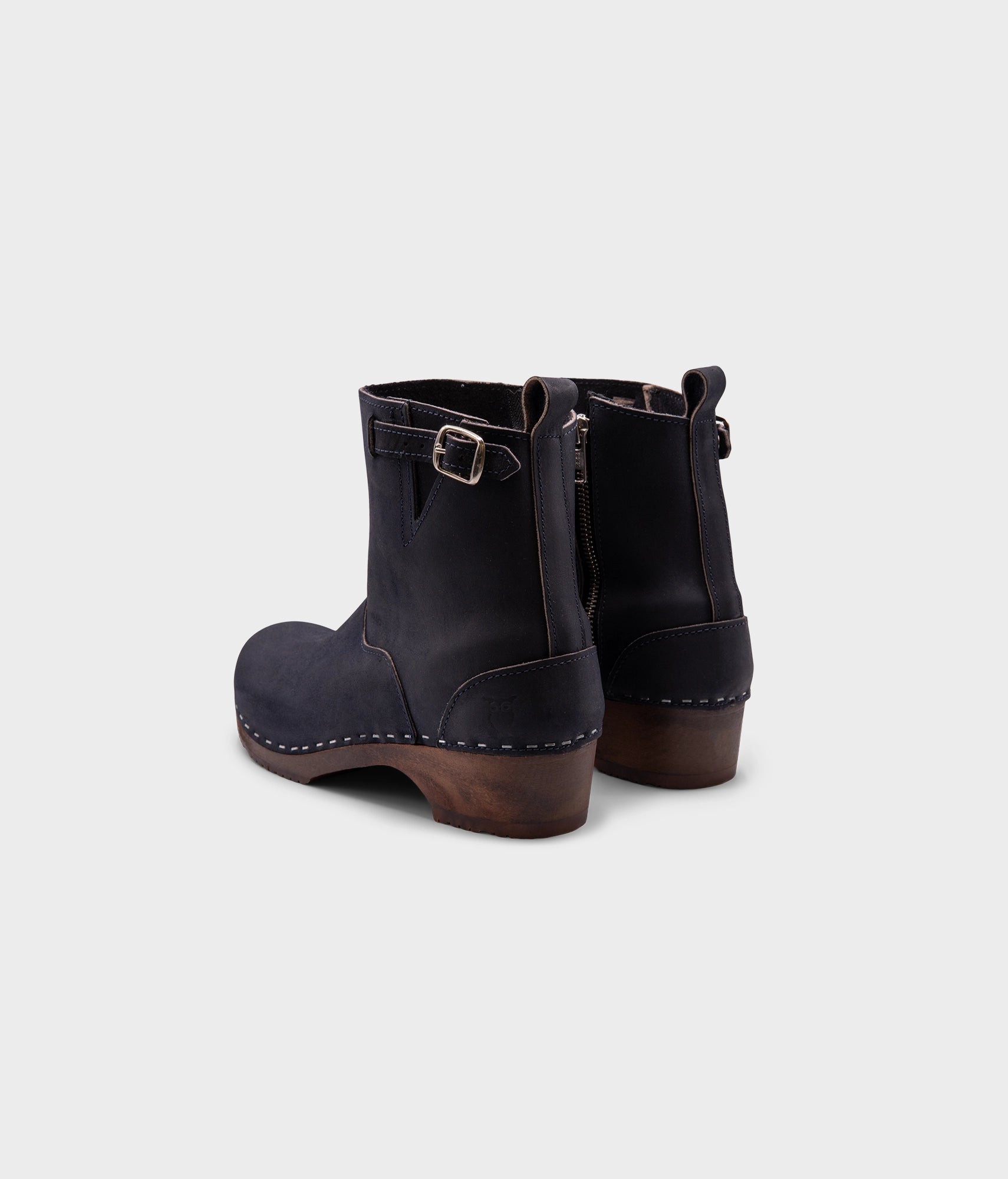 low heeled clog boots in navy blue nubuck leather with a mid-shaft and silver buckle, stapled on a dark wooden base