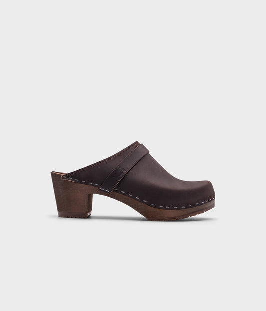 classic high heeled clog mule in dark brown nubuck leather stapled on a dark wooden base with a leather strap