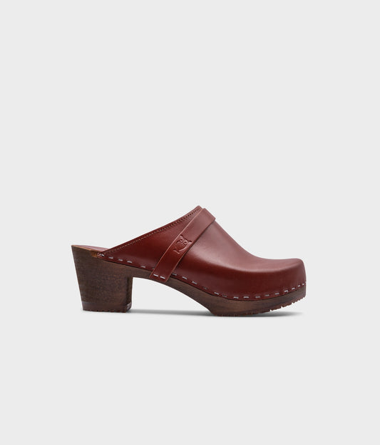 classic high heeled clog mule in cognac red vegetable tanned leather stapled on a dark wooden base with a leather strap