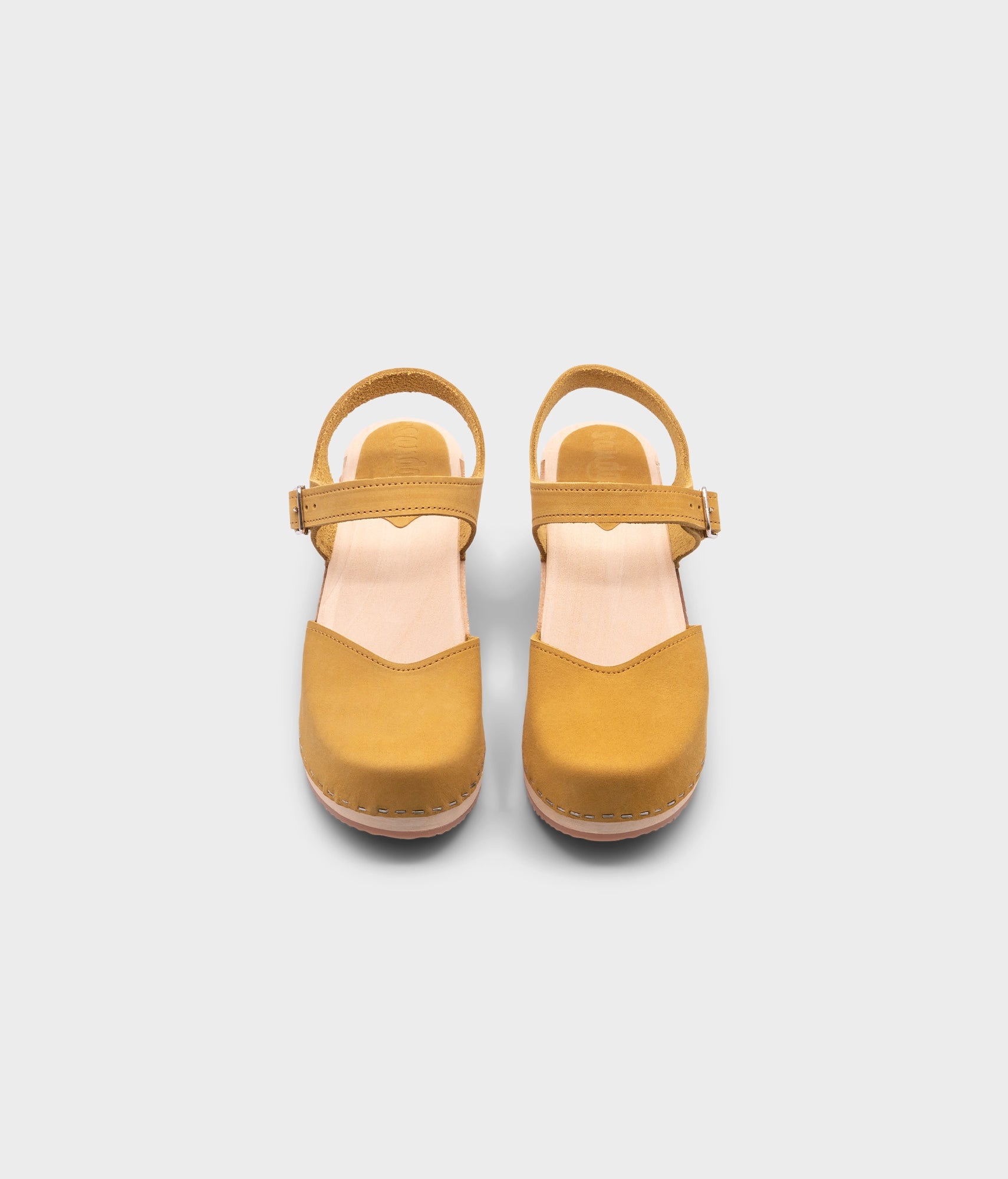 high-heeled clog sandals with a closed toe in yellow leather stapled on a light wooden base