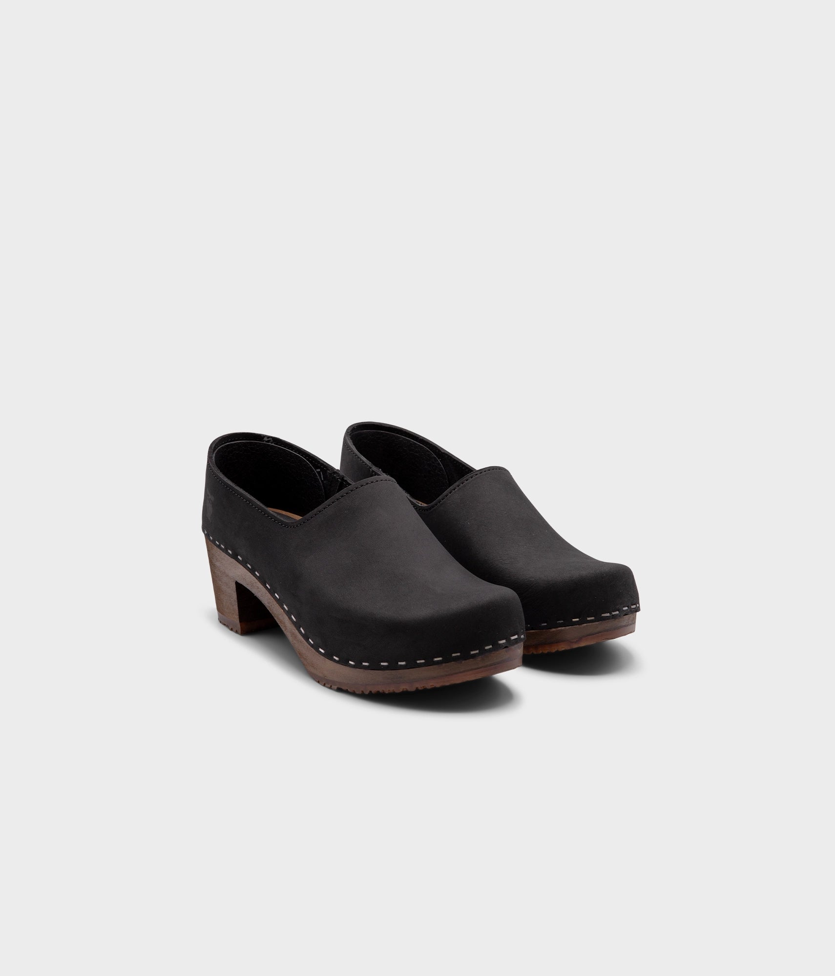 high heeled closed-back clogs in black nubuck leather stapled on a dark wooden base