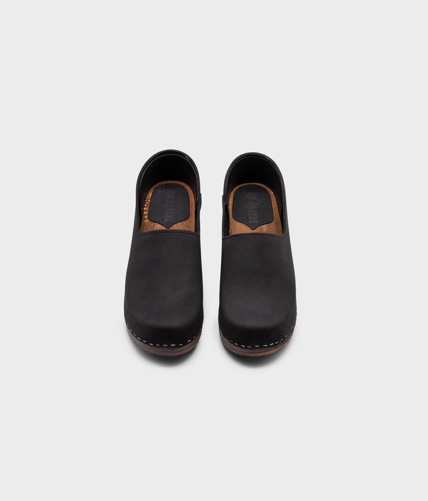 high heeled closed-back clogs in black nubuck leather stapled on a dark wooden base