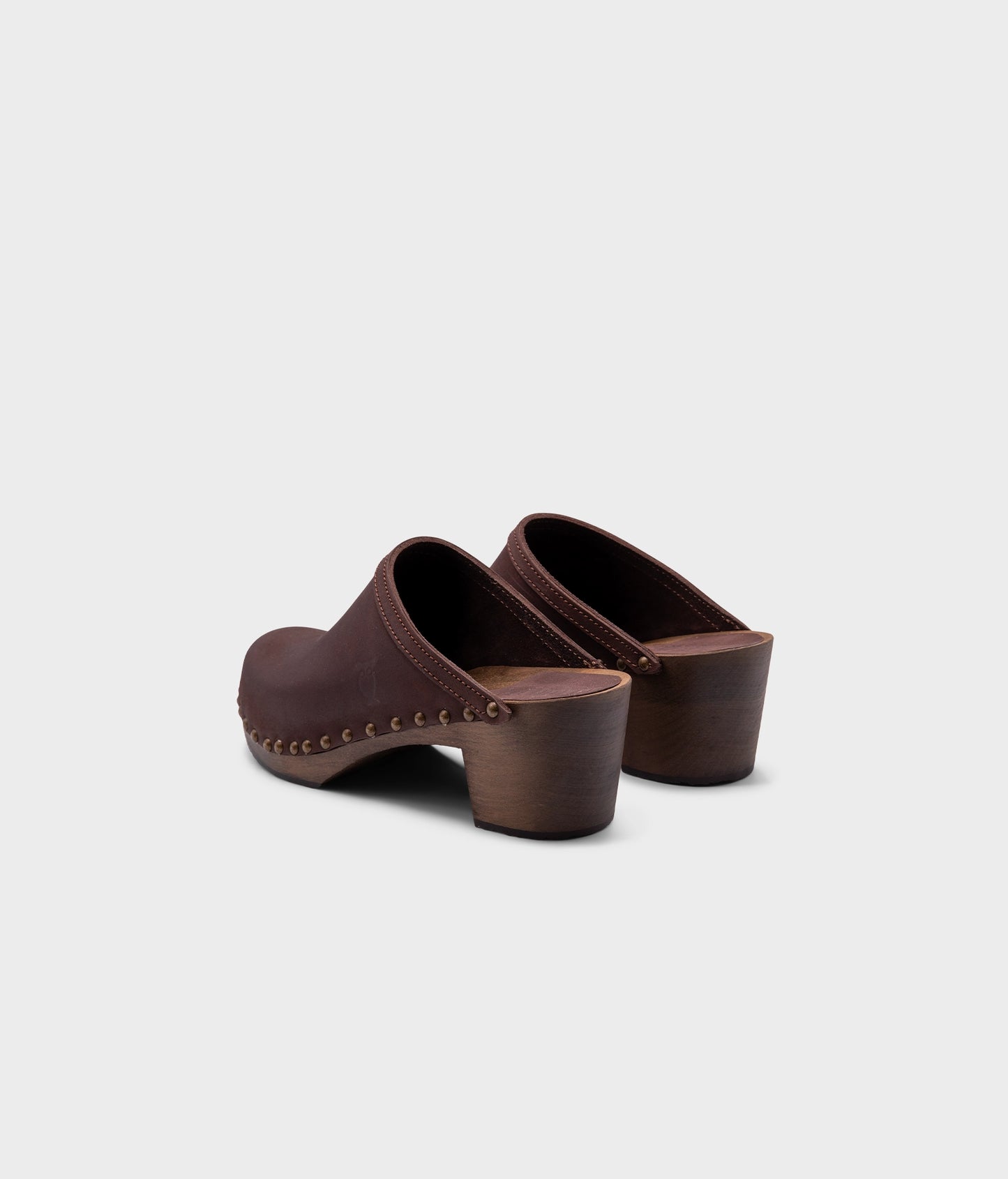 high heeled clog mules in dark brown nubuck leather stapled on a dark wooden base with brass gold studs