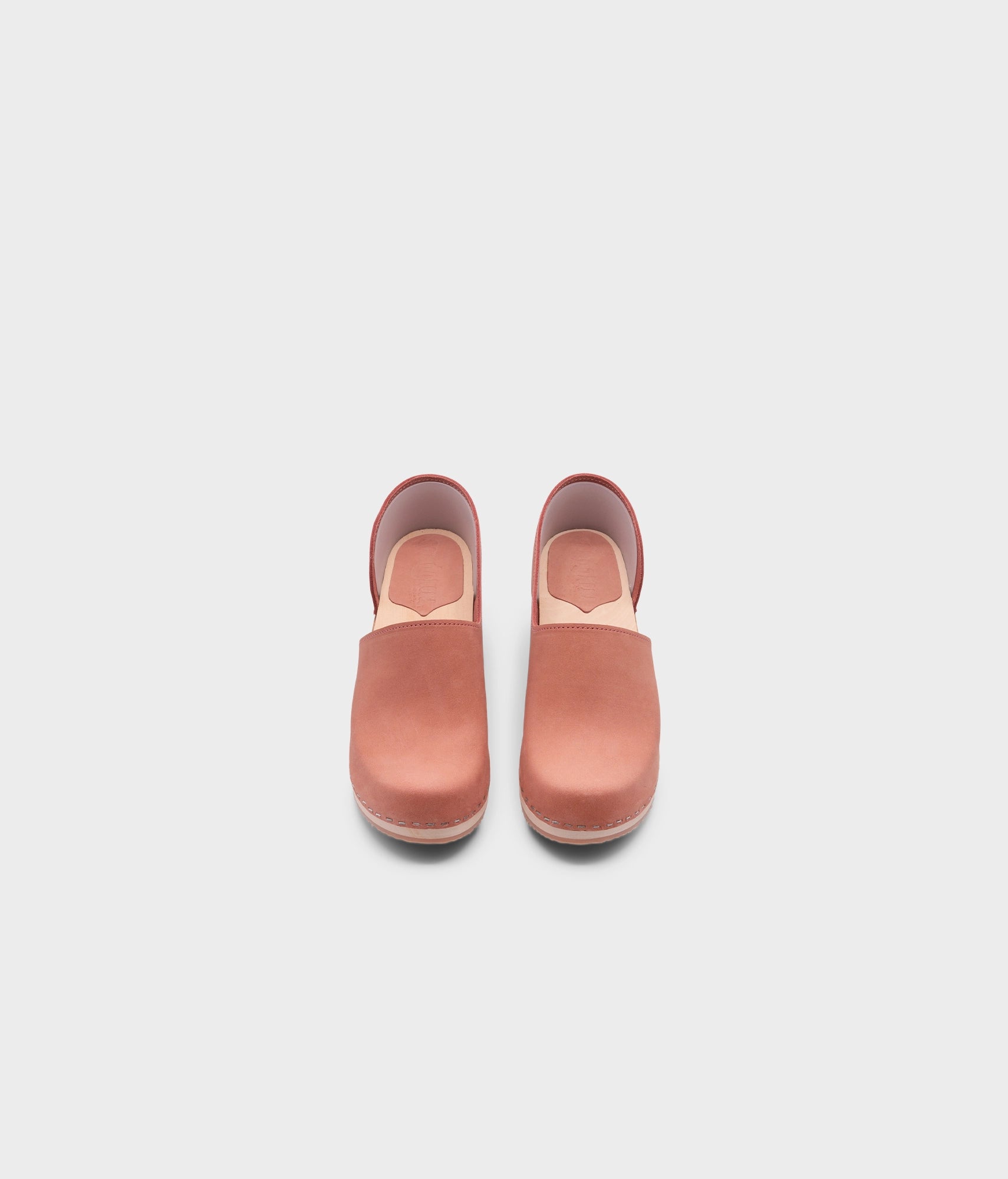 high heeled closed-back clogs in blush pink nubuck leather stapled on a light wooden base