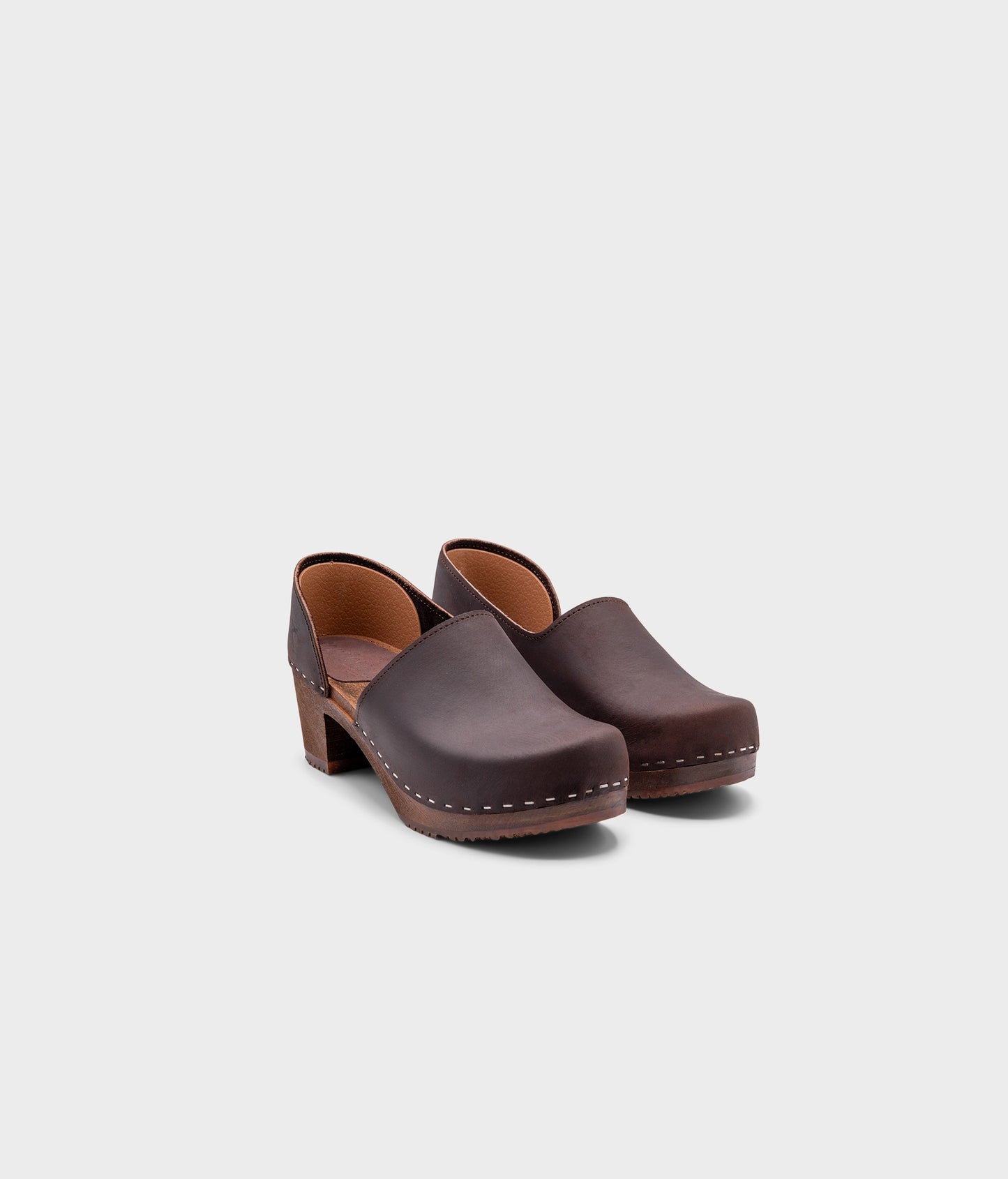 high heeled closed-back clogs in dark brown nubuck leather stapled on a dark wooden base