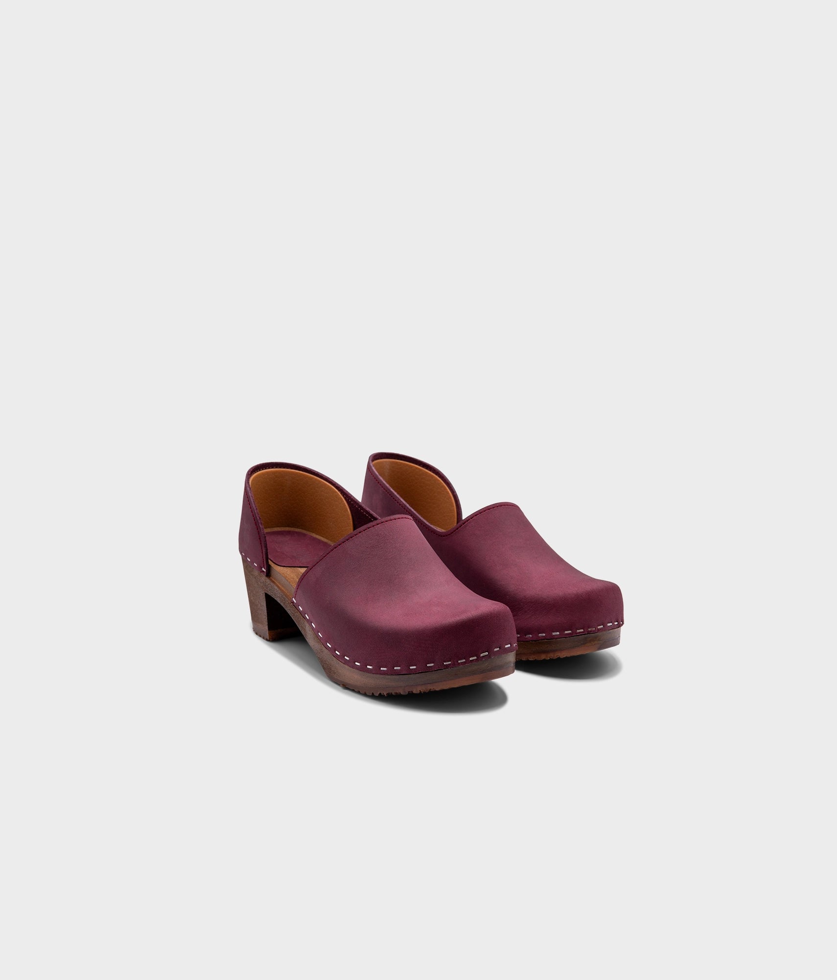 high heeled closed-back clogs in purple plum nubuck leather stapled on a dark wooden base