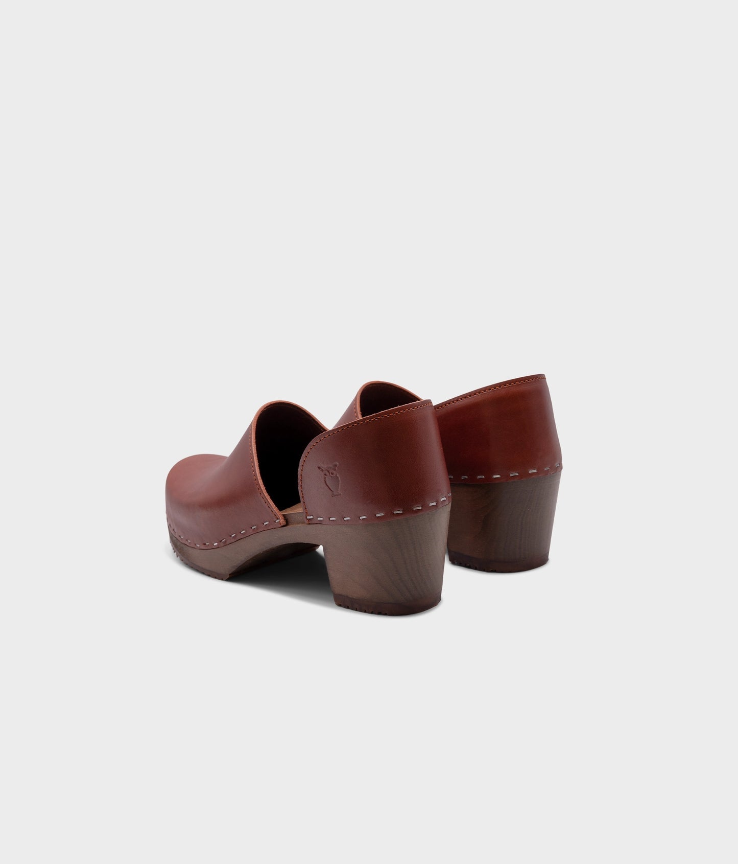 high heeled closed-back clogs in cognac red vegetable tanned leather stapled on a dark wooden base