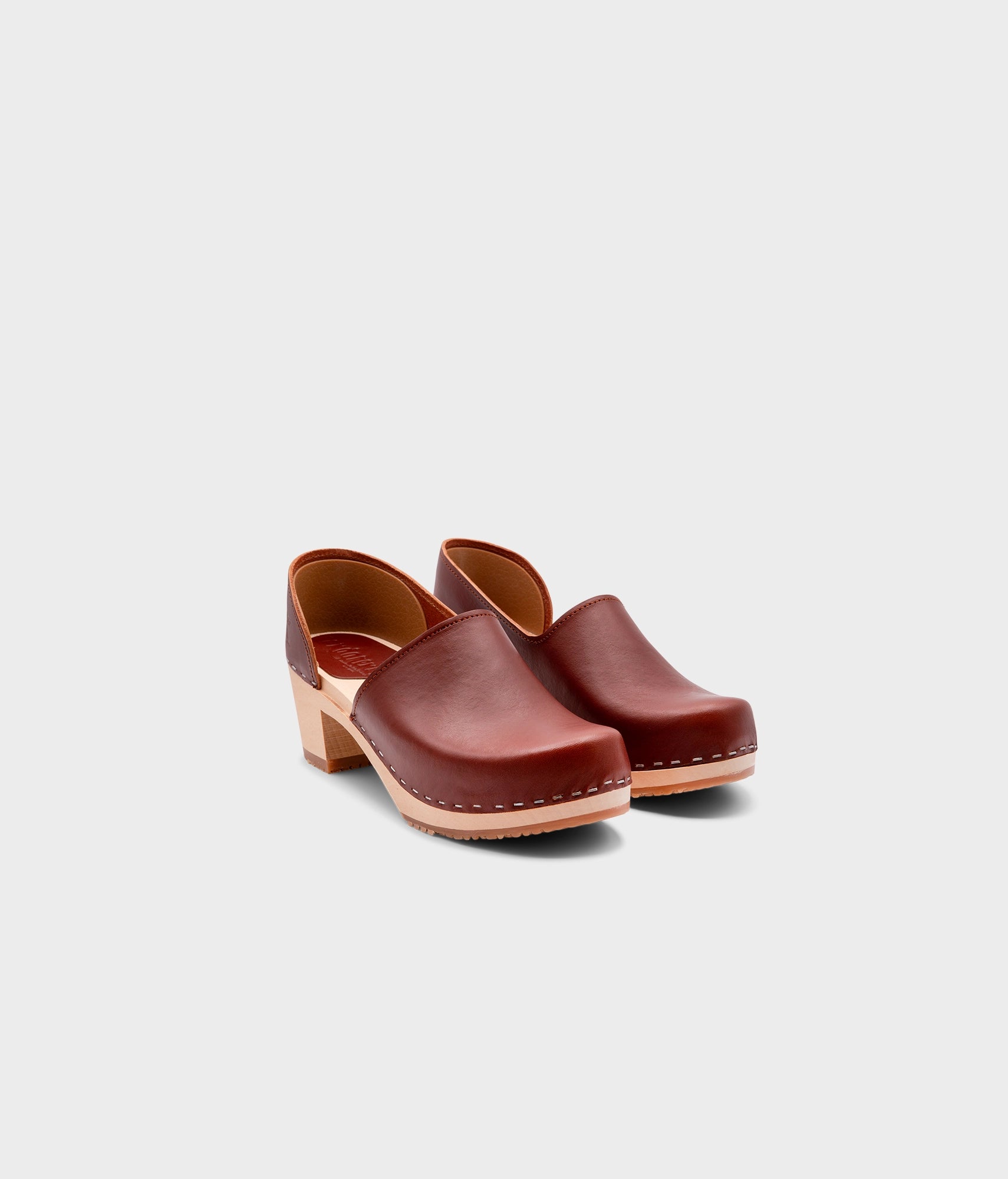high heeled closed-back clogs in red cognac vegetable tanned leather stapled on a light wooden base