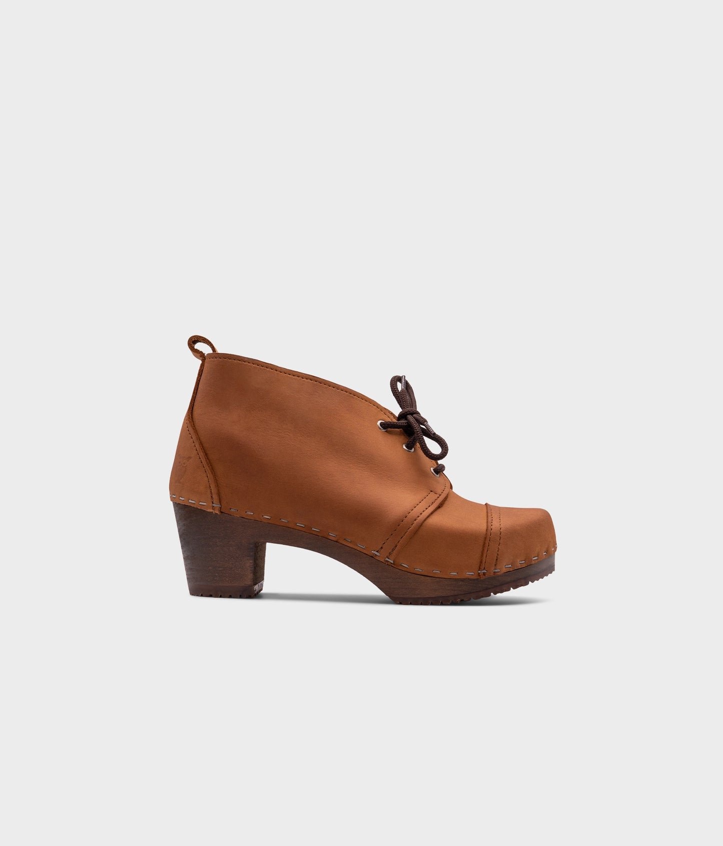 high heeled chukka clog boots in light brown nubuck leather stapled on a dark wooden base with brown laces