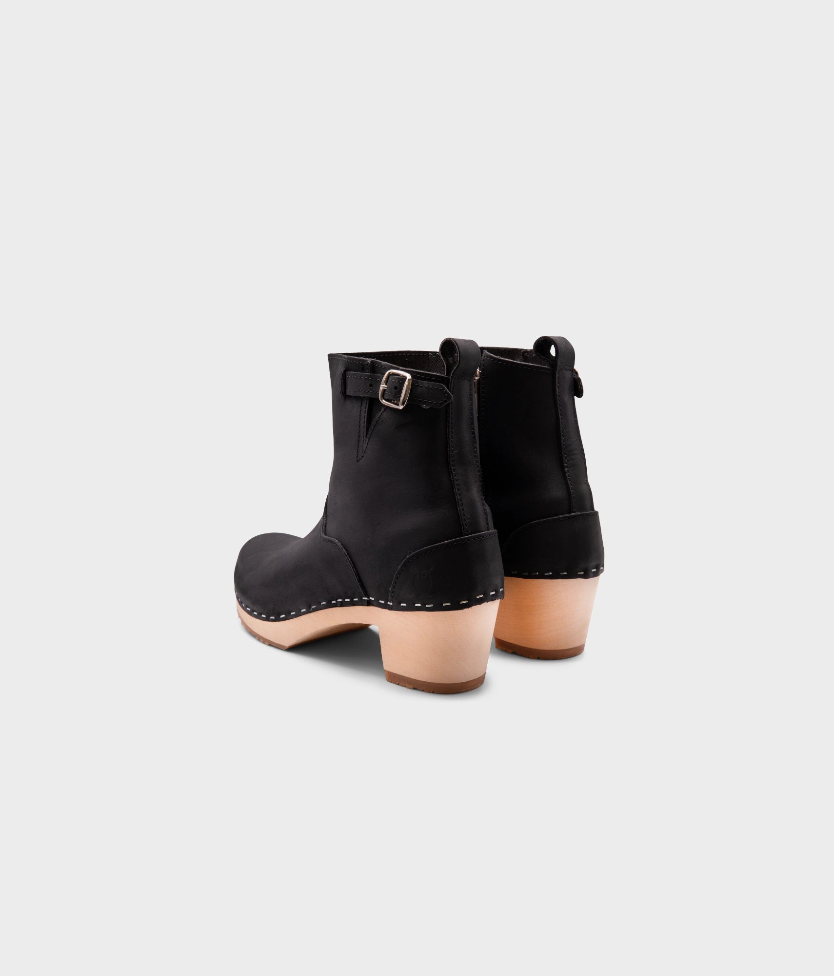 high-heeled clog boots in black nubuck leather stapled on a light wooden base with a silver buckle