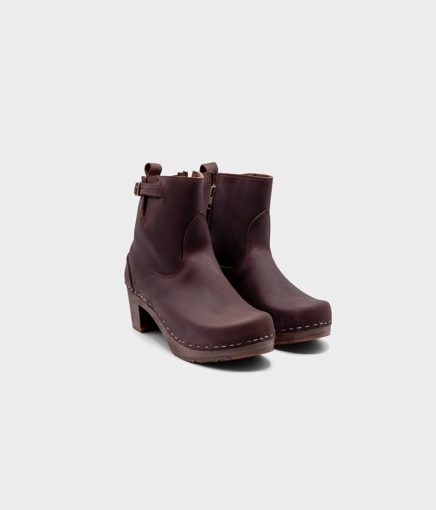 high-heeled clog boots in dark brown nubuck leather stapled on a dark wooden base with a silver buckle