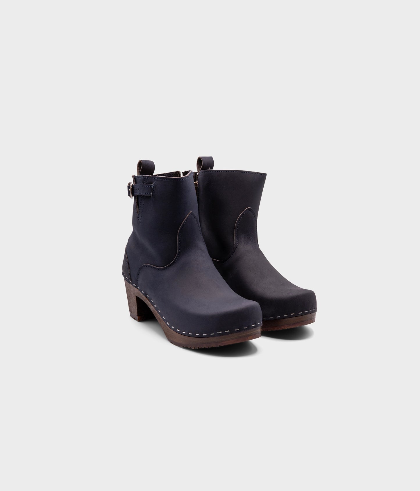 high-heeled clog boots in navy blue nubuck leather stapled on a dark wooden base with a silver buckle