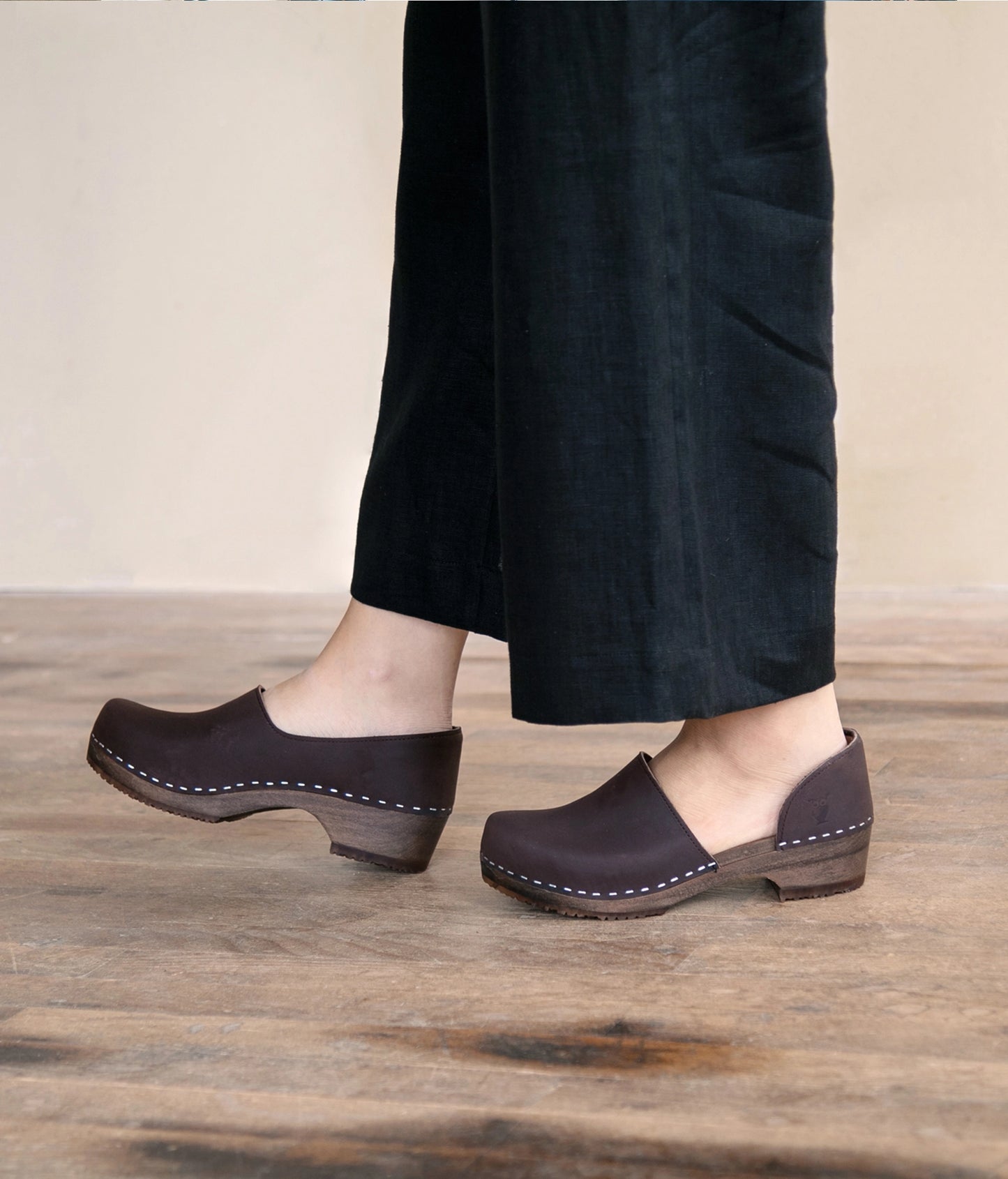 low heeled closed-back clogs in dark brown nubuck leather stapled on a dark wooden base