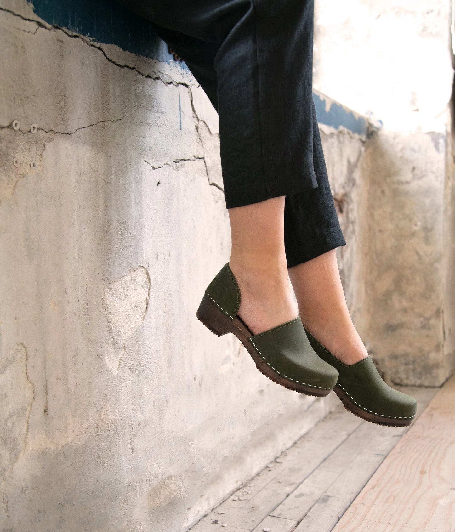 Legs over a wall with Sandgrens Brett Swedish clogs in Olive Nubuck