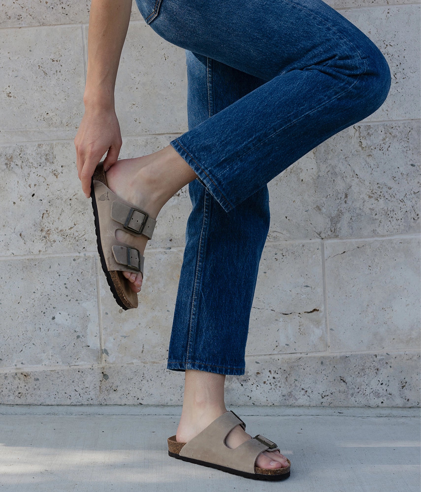 woman wearing dark blue jeans along with a pair of classic cork sandals in beige nubuck leather with a brown EVA sole, suede footbed and brass gold buckle