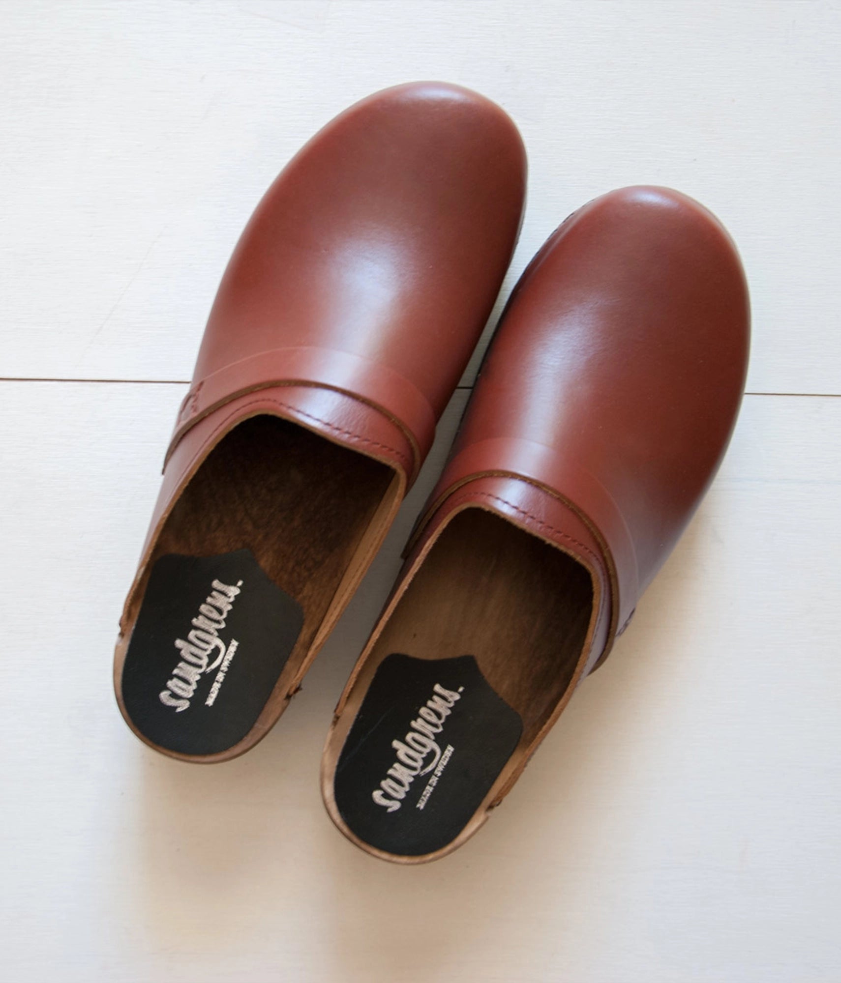 low heeled classic clog mules in cognac red vegetable tanned leather stapled on a dark wooden base