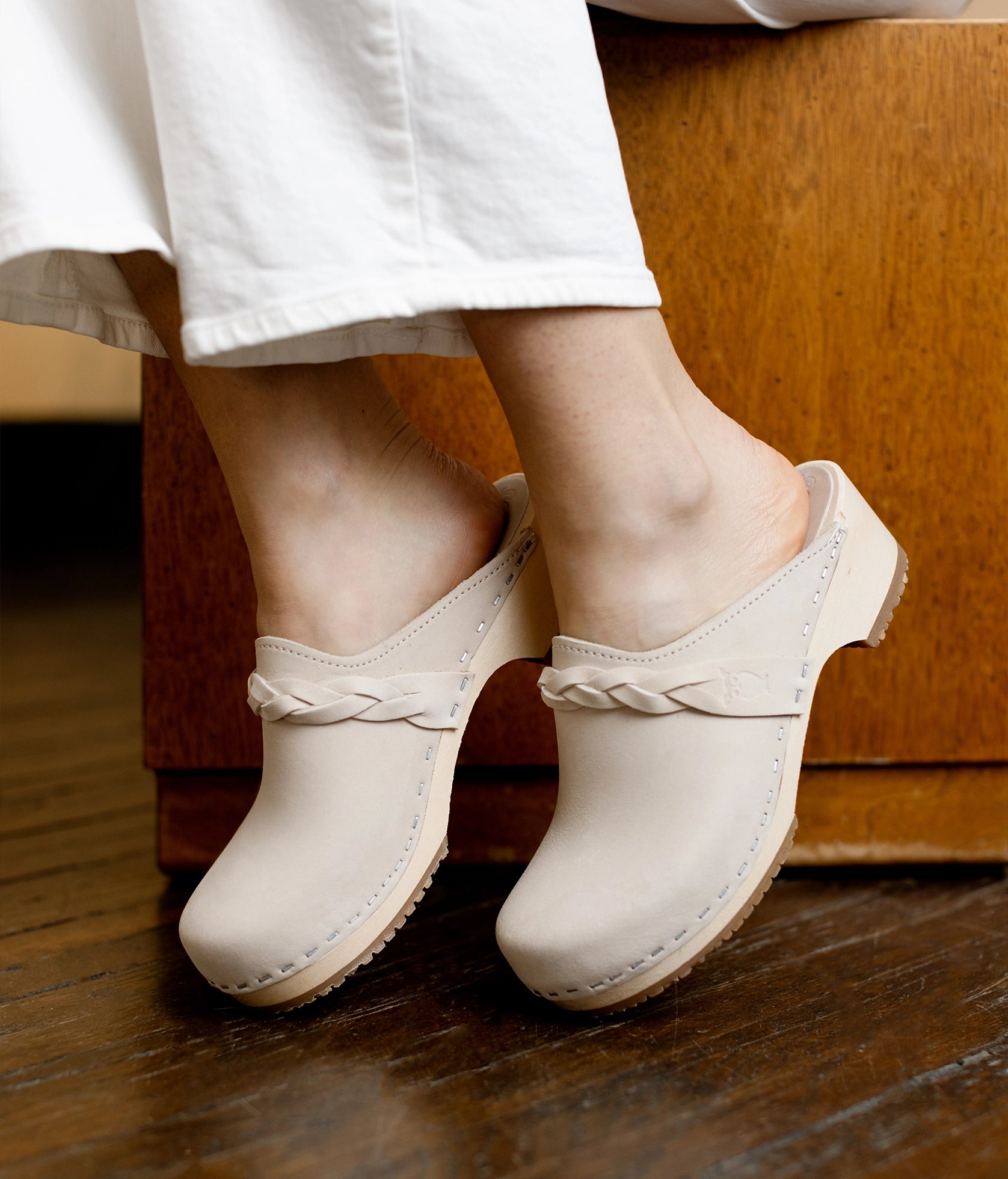 low heeled clog mules in sand white nubuck leather with a braided strap stapled on a light wooden base