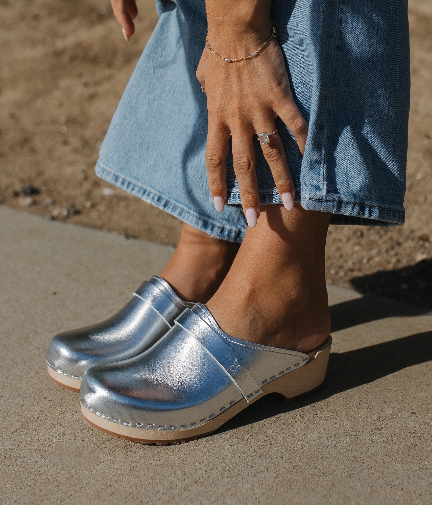 classic low heeled clog mule in metallic silver traditional leather stapled on a light wooden base with a leather strap