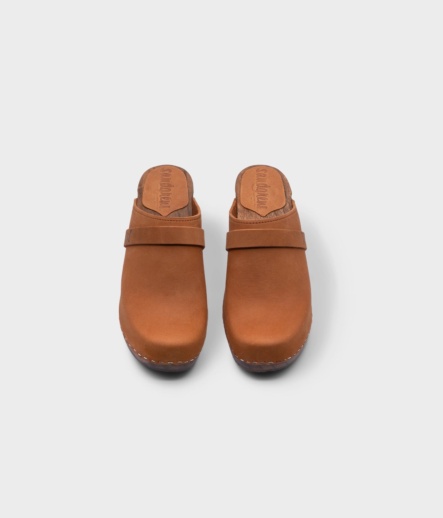 classic high rise heel clog mule in light brown nubuck leather stapled on a dark wooden base