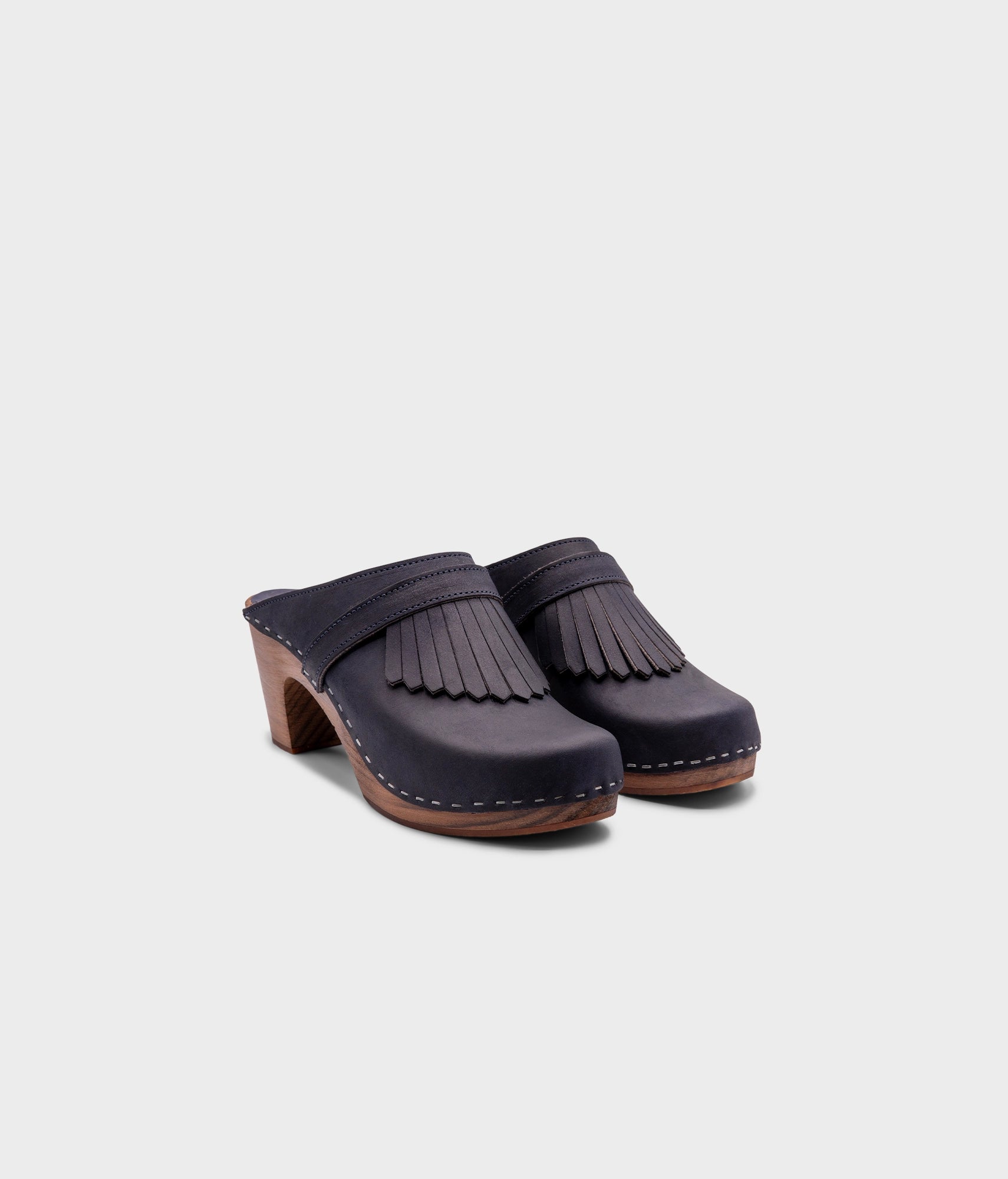 high rise clog mule in navy blue nubuck leather stapled on a dark wooden base with a leather strap with fringes