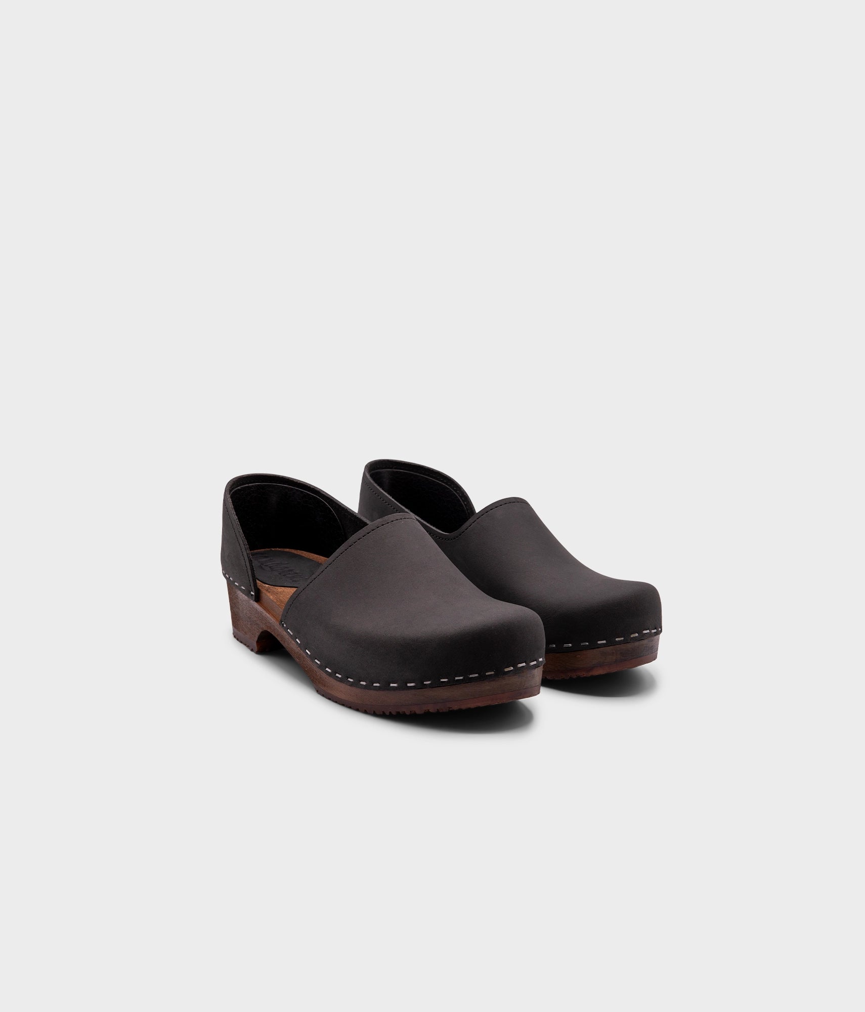 low heeled closed-back clogs in black nubuck leather stapled on a dark wooden base