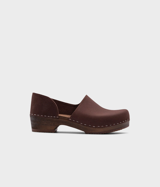 low heeled closed-back clogs in dark brown nubuck leather stapled on a dark wooden base