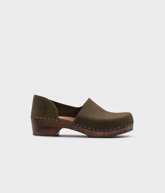 low heeled closed-back clogs in olive green nubuck leather stapled on a dark wooden base