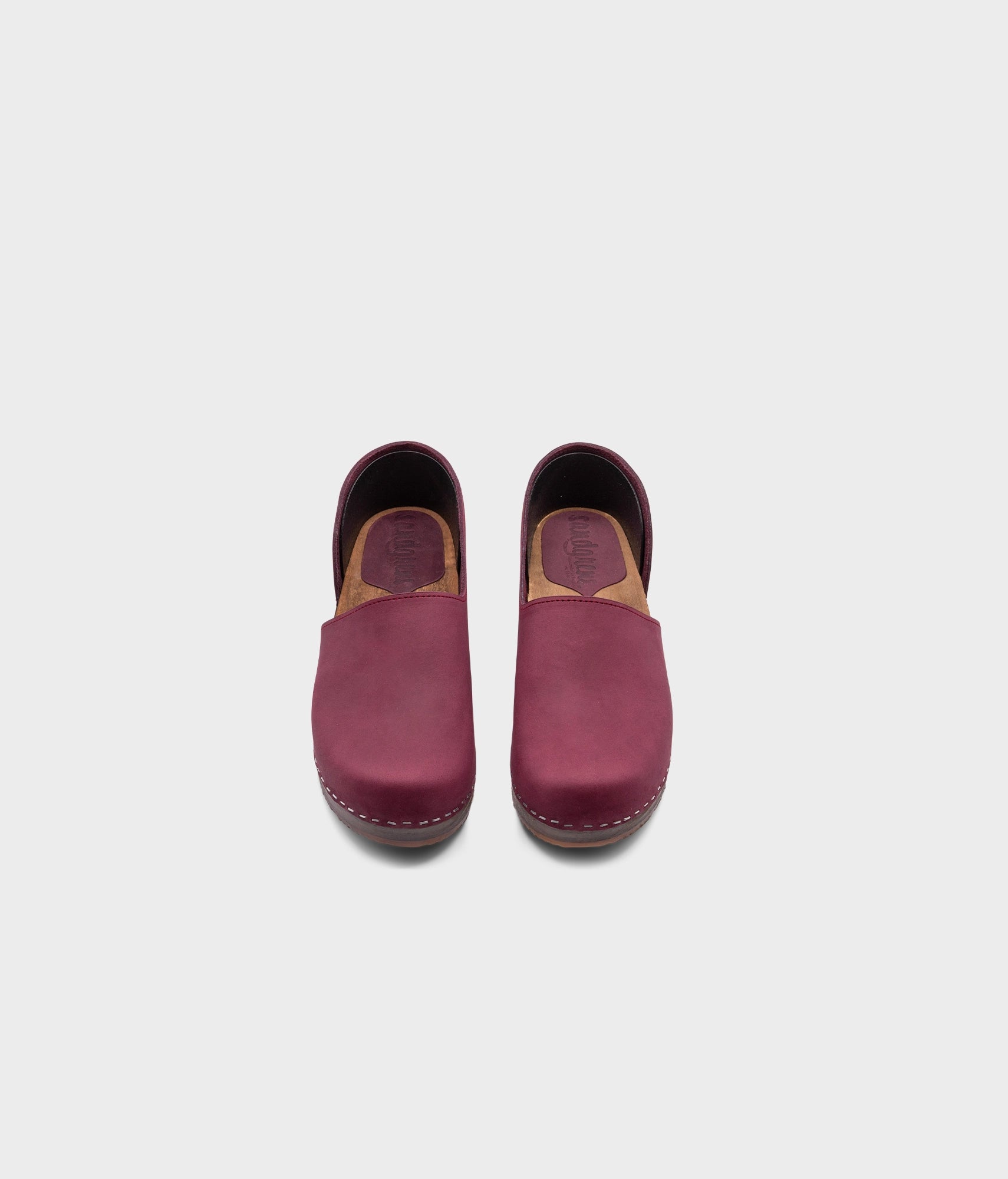 low heeled closed-back clogs in dark purple nubuck leather stapled on a dark wooden base