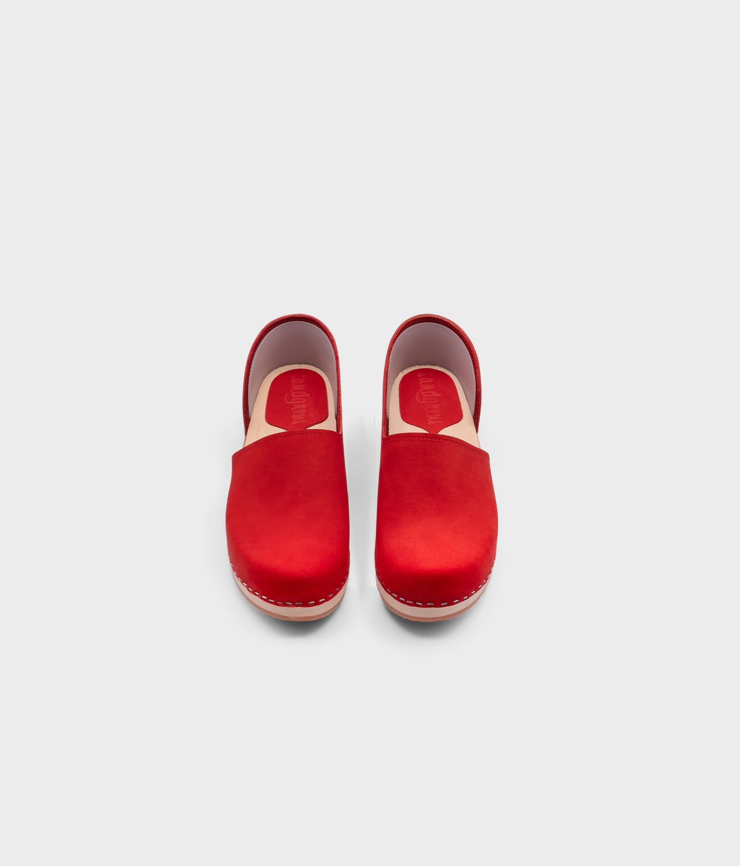 low heeled closed-back clogs in red nubuck leather stapled on a light wooden base